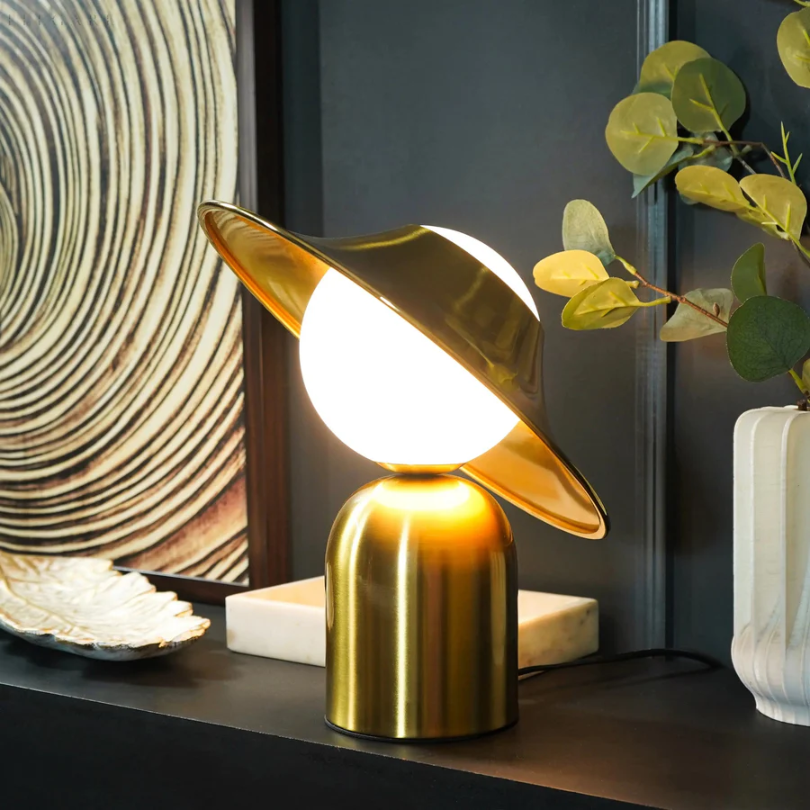 Elegancka metalowa lampa stołowa w złotym kolorze z odchyloną głowicą i ciepłym światłem