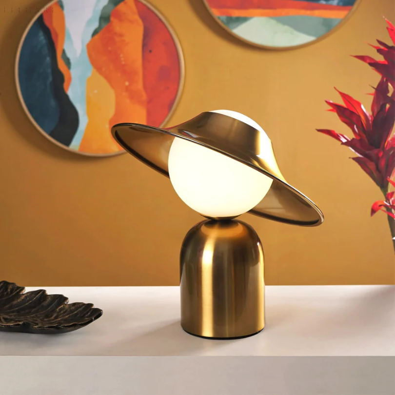 Elegancka metalowa lampa stołowa w złotym kolorze z odchyloną głowicą i ciepłym światłem